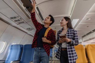 Genç bir çift uçakta bir uçuş için hazırlanıyor. Kadın gülümseyip pasaportlarını tutarken erkek bavullarını başındaki kutuya koyar. İkisi de yolculuklarına başlamak için heyecanlı görünürler..