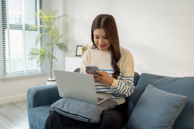 Genç bir kadın koltukta rahat bir şekilde oturur, önünde dizüstü bilgisayarıyla gülümserken dijital yaşam tarzı, bağlantı ve modern iş dengesini temsil eder..