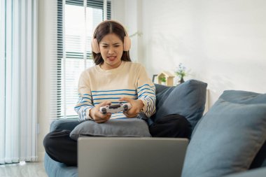 Kulaklık takan genç bir kadın dizüstü bilgisayarında video oyunu oynuyor. Oyun sırasında duygusal ifadeler, heyecan ve hüsran içeren bir kumanda taşıyor..