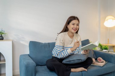 Evdeki kanepede oturan genç bir kadın elinde bir kitapla rahatlıyor. Okumaktan zevk alırken sakin ve mutlu görünüyor, boş zamanı ve huzurlu yaşam tarzını temsil ediyor..