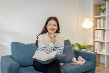 Evdeki kanepede oturan genç bir kadın elinde bir kitapla rahatlıyor. Okumaktan zevk alırken sakin ve mutlu görünüyor, boş zamanı ve huzurlu yaşam tarzını temsil ediyor..