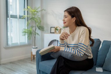 Evdeki kanepede oturan genç bir kadın elinde bir kitapla rahatlıyor. Okumaktan zevk alırken sakin ve mutlu görünüyor, boş zamanı ve huzurlu yaşam tarzını temsil ediyor..