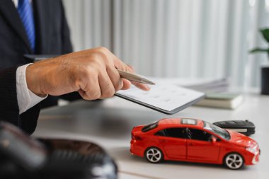 Takım elbiseli bir işadamı, masasında minyatür araba modelleri olan araç sigortası, finansal planlama ve yasal anlaşmaları sembolize eden araba sigortası ve sözleşme belgeleri sunuyor..
