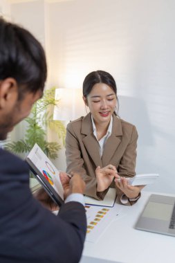 İki iş adamı modern bir ofiste finansal çizelge ve stratejileri tartışıyor. Resmi bir toplantıda fikir alışverişinde bulunur, raporları analiz eder ve çözümleri müzakere ederler..