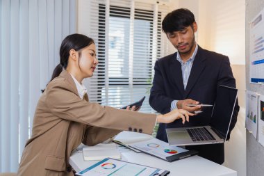 İş arkadaşları aktif olarak ortak bir toplantıda, çizelgeleri gözden geçiriyorlar, verilere işaret ediyorlar ve fikir alışverişinde bulunuyorlar. Takım çalışmaları strateji planlaması, analiz ve işbirliğini yansıtır..