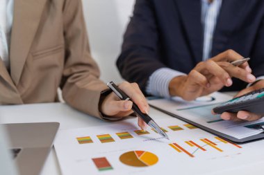 İki iş adamı, modern bir ofiste mali tablolar ve raporları tartışıyor. Birlikte çalışırlar, fikirleri paylaşırlar ve birlikte verileri analiz ederler, takım çalışmasını ve stratejisini vurgularlar..