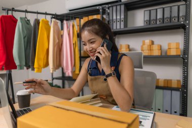 Genç bayan girişimci telefonda konuşurken gülümsüyor ve evde dizüstü bilgisayar kullanıyor. Bir internet mağazası işletiyor, siparişleri kontrol ediyor ve e-ticaret işi için müşterilerle iletişim kuruyor..