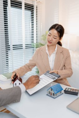 İki iş adamı emlak yatırımını tartışıyor, emlak sözleşmeleri imzalıyor ve ev modellerini gözden geçiriyor, konut satışlarını, finansmanı ve başarılı anlaşmaları sembolize ediyor.