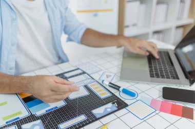 Bir erkek tasarımcı UX UI görevlerine odaklanmış, kablolar, çizimler ve renk paletleri olan uygulama prototipleri yaratıyor. Kullanıcı arayüzünü ve kullanılabilirliğini optimize etmek için yaratıcı fikirlerle çalışıyor..