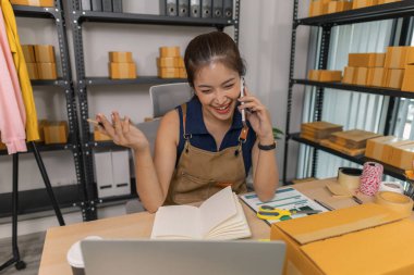 Genç bayan girişimci telefonda konuşurken gülümsüyor ve evde dizüstü bilgisayar kullanıyor. Bir internet mağazası işletiyor, siparişleri kontrol ediyor ve e-ticaret işi için müşterilerle iletişim kuruyor..