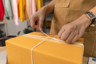 Karton bir kutunun etrafına ip bağlayan genç bir kadının yakın plan fotoğrafları. Online bir iş yürütüyor. Detaylara dikkat eden müşterilere teslimat için paketleri dikkatlice hazırlıyor.