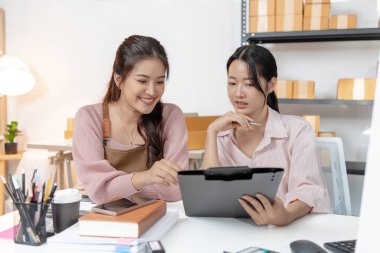 Küçük bir ofiste birlikte çalışan iki genç kadın, belgeleri tartışıyor ve iş verilerini gözden geçiriyorlar. Takım çalışmaları modern bir çalışma alanında işbirliği, planlama ve üretkenliği vurguluyor.