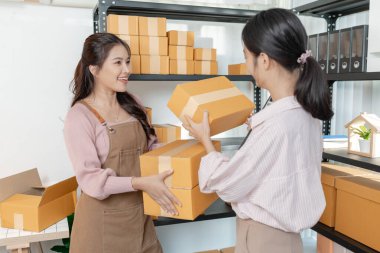 Küçük bir işletme ofisinde birlikte çalışan iki genç kadın, karton kutular hazırlıyor, envanter kontrolü yapıyor ve yeni açılan çevrimiçi mağaza operasyonlarının bir parçası olarak ambalaj işlerini yürütüyorlar..