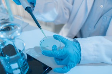 Beyaz laboratuvar önlüklü iki kadın bilim adamı, takım çalışmasını ve modern bilimsel araştırma ortamını temsil eden mikroskoplar, cam eşyalar ve mavi test tüpleriyle parlak bir laboratuvarda birlikte çalışıyorlar..