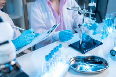 Bilimsel ekipmanlar, bilgisayarlar ve cam eşyalar ile çevrili modern bir laboratuvarda birlikte çalışan beyaz önlüklü iki kimyager, bilimsel araştırmalarda takım çalışmasını temsil ediyor..