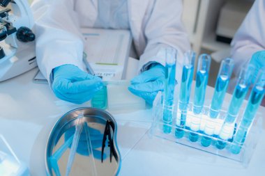 Bilimsel ekipmanlar, bilgisayarlar ve cam eşyalar ile çevrili modern bir laboratuvarda birlikte çalışan beyaz önlüklü iki kimyager, bilimsel araştırmalarda takım çalışmasını temsil ediyor..