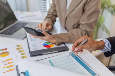 İki iş adamı, modern bir ofiste mali tablolar ve raporları tartışıyor. Birlikte çalışırlar, fikirleri paylaşırlar ve birlikte verileri analiz ederler, takım çalışmasını ve stratejisini vurgularlar..