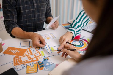 UX / UI tasarımcılarından oluşan bir grup, modern bir tasarım ofisinde yeni mobil uygulama arayüzü için renk paletleri ve konseptleri tartışarak yaratıcı fikirler üzerinde birlikte beyin fırtınası yapıyorlar..