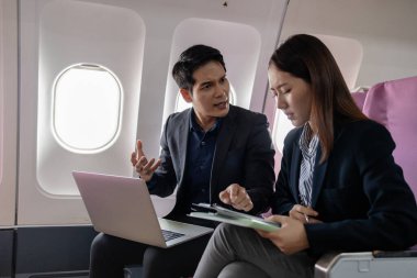 İki Asyalı iş adamı uçuş sırasında iş konuşuyorlar, bir uçak kabininde oturuyorlar. Kadın elinde belgelerle kalem tutarken adam ciddi bir şekilde el kol hareketi yapıyor..