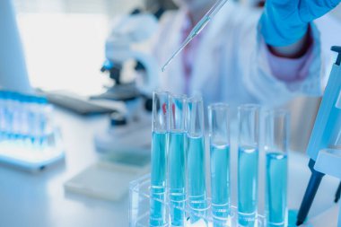 Beyaz laboratuvar önlüklü iki kadın bilim adamı, takım çalışmasını ve modern bilimsel araştırma ortamını temsil eden mikroskoplar, cam eşyalar ve mavi test tüpleriyle parlak bir laboratuvarda birlikte çalışıyorlar..