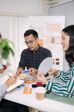 UX / UI tasarımcılarından oluşan bir grup, modern bir tasarım ofisinde yeni mobil uygulama arayüzü için renk paletleri ve konseptleri tartışarak yaratıcı fikirler üzerinde birlikte beyin fırtınası yapıyorlar..