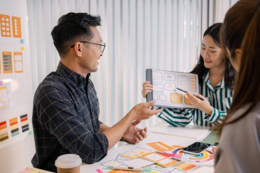 Mobil uygulama düzeni ve kullanıcı akışını iyileştirmek için UX / UI planlama toplantısı düzenleyen tasarımcılar. İşlevsel ve görsel arayüz çözümleri yaratmak için yakın işbirliği yaparlar..