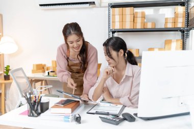 Küçük bir iş ofisinde birlikte çalışan iki genç kadın paketleri düzenliyor, belgeleri gözden geçiriyor ve gülümseyerek görevler planlıyorlar. Sahne takım çalışması, üretkenlik ve modern girişimciliği yansıtır