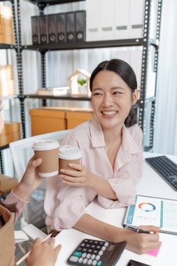 Küçük bir ofiste birlikte çalışan iki genç kadın, belgeleri tartışıyor ve iş verilerini gözden geçiriyorlar. Takım çalışmaları modern bir çalışma alanında işbirliği, planlama ve üretkenliği vurguluyor.