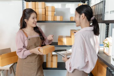 Küçük bir işletme ofisinde birlikte çalışan iki genç kadın, karton kutular hazırlıyor, envanter kontrolü yapıyor ve yeni açılan çevrimiçi mağaza operasyonlarının bir parçası olarak ambalaj işlerini yürütüyorlar..