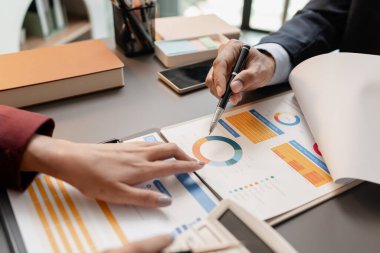 Modern bir ofis masasında toplanan iş adamları, planlar ve bütçe raporlarını gözden geçirirken, aynı zamanda yaklaşan iş kararları için temel mali içgörüler ve stratejik planlar üzerinde de tartıştılar..