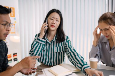 Bir ekibin tasarım sorunları ve proje zorluklarını tartıştığı gergin bir iş toplantısı. Bir ekip üyesi iş yeri baskısı ve takım çalışması göstererek stresli görünürken, adam çözümleri açıklamaya çalışıyor