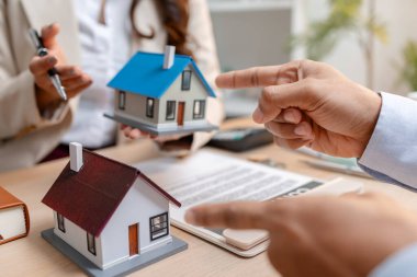 Bir emlakçı ve bir müşteri, emlak satın alma toplantısı sırasında bir konut sözleşmesi belgesini tartışıyor ve ona ev sahipliği hakkında anlaşma detayları ve mali müzakereleri gösteriyorlar.