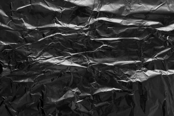 Shiny black foil texture background, pattern of wrapping paper with crumpled and wavy.