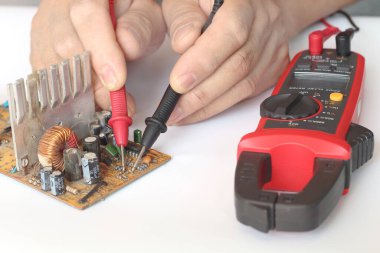 Elektronik devreyi tamir eden erkeklerin ellerini kapat. Devre kartı çoklu metre testçi ile..