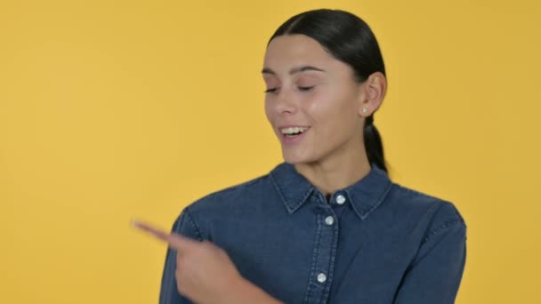 Mujer latina joven señalando el producto, fondo amarillo — Vídeo de stock