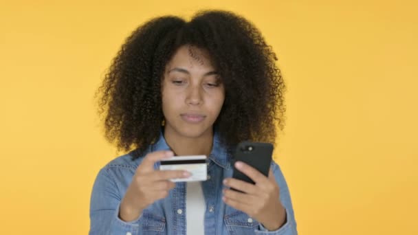 Онлайн-покупки на смартфоне от молодой африканки, жёлтый фон — стоковое видео