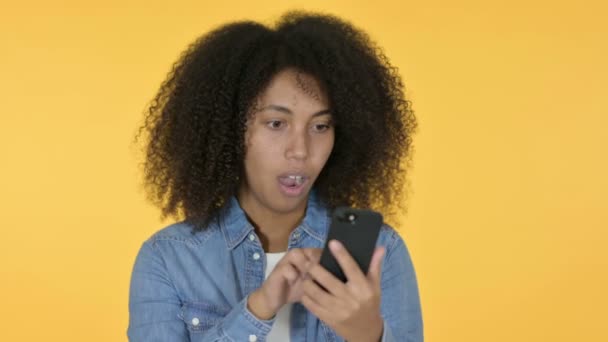 Junge Afrikanerin verliert auf Smartphone, gelbem Hintergrund — Stockvideo