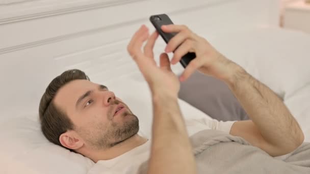 Smartphone-Nutzung durch jungen Mann im Bett — Stockvideo