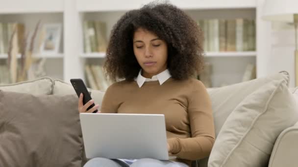 Mladá africká žena pracující na Smartphone a notebook na pohovce — Stock video
