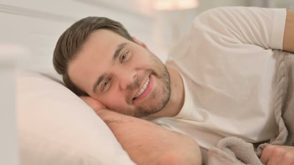 Retrato de un joven acostado en la cama sonriendo ante la cámara — Vídeos de Stock