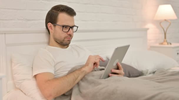 Ontspannende jonge man met behulp van Tablet in bed — Stockvideo
