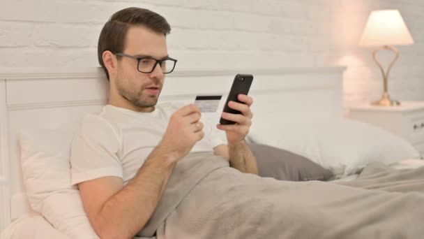 Erfolgreicher Online-Einkauf per Smartphone durch jungen Mann im Bett — Stockvideo