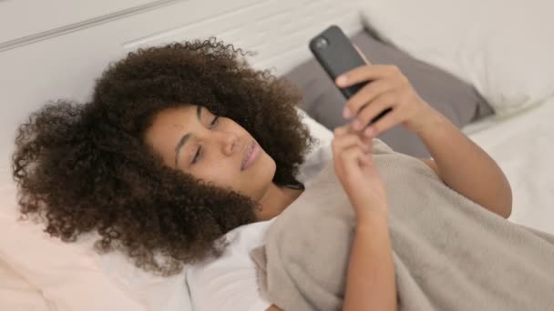 Smartphone-Nutzung durch Afrikanerin, die im Bett liegt — Stockvideo