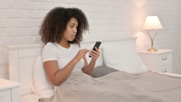 Erfolg: Afrikanerin feiert auf Smartphone im Bett — Stockvideo