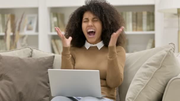 Emocionada joven africana con ordenador portátil celebrando en el sofá — Vídeos de Stock