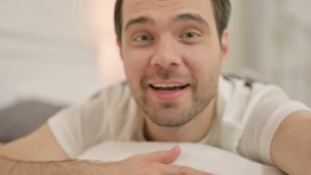 Закрыть привлекательный молодой человек в видеочате в постели — стоковое видео
