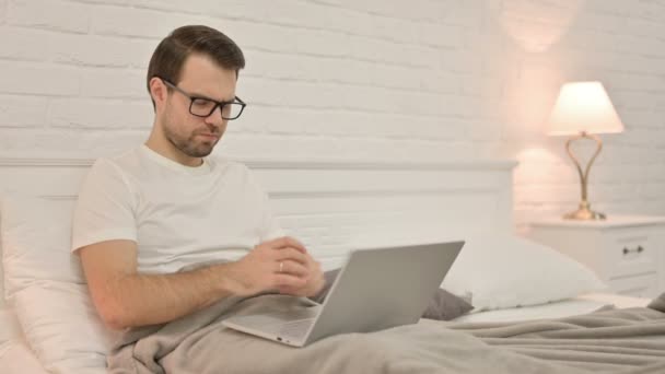 Jeune homme avec ordinateur portable ayant la douleur au poignet au lit — Video