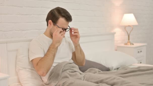 Junger Mann sitzt mit Kopfschmerzen im Bett — Stockvideo