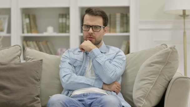 Lässiger junger Mann sitzt und denkt zu Hause — Stockvideo