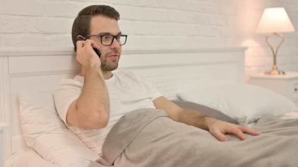 Jonge man aan het praten op Smartphone in bed — Stockvideo
